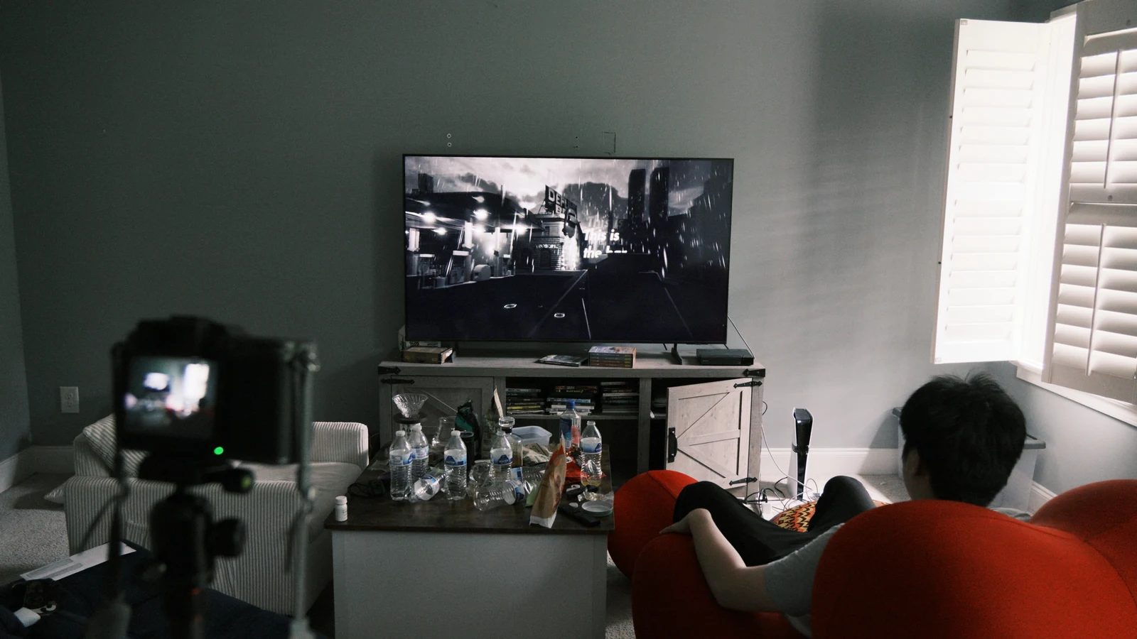 An in-game living room with a camera, a television and a red chair.